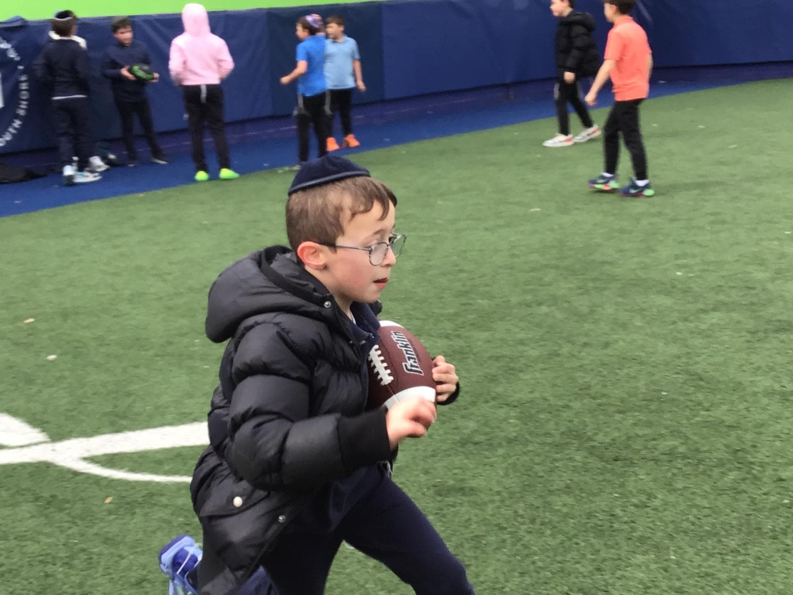 A boy running with a football on the turf field